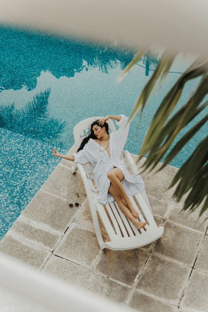 Woman in a bathrobe lounging by a serene poolside, enjoying a relaxing moment.