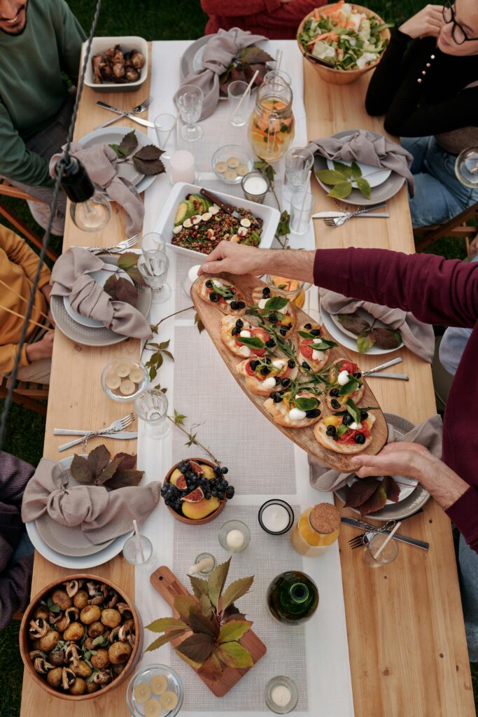 A lively outdoor meal gathering with a diverse array of dishes on a wooden table.